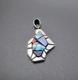 A Southwestern-style silver pendant featuring a geometric inlay of turquoise, lapis lazuli, and a small red accent stone, displayed on a dark gray textured background.
